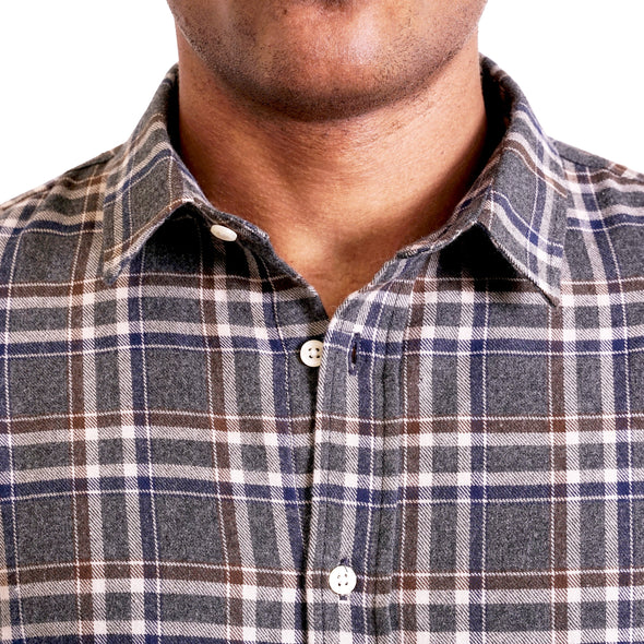 close up view of the collar and neck area of woven button up shirt showing off the pointed collar and gray plaid flannel fabric on a black male model